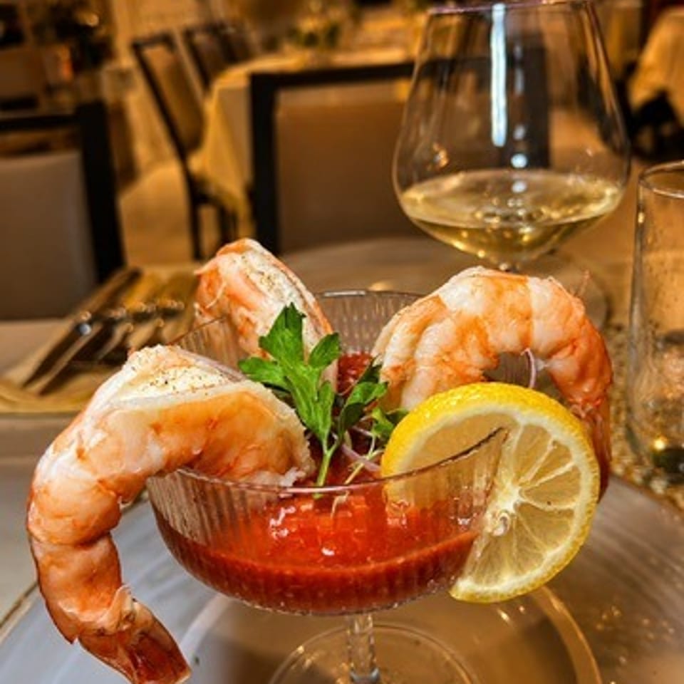 Shrimp cocktail with jumbo prawns, red sauce, lemon garnish, and parsley on a restaurant table.