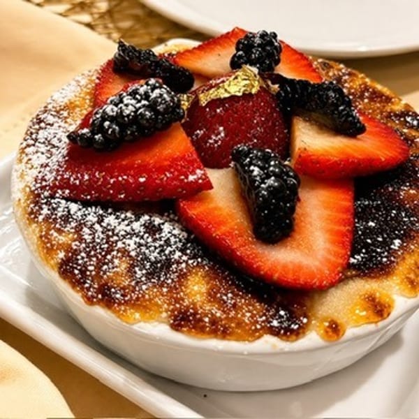 Golden-browned dessert topped with sliced strawberries, blackberries, powdered sugar, and edible gold leaf.