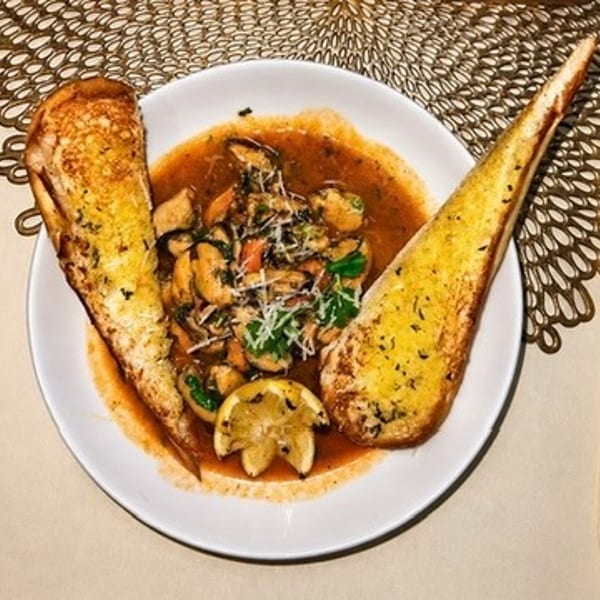 Plate of shrimp and mushrooms in tomato sauce, garnished with herbs and cheese, served with two slices of toasted garlic bread.
